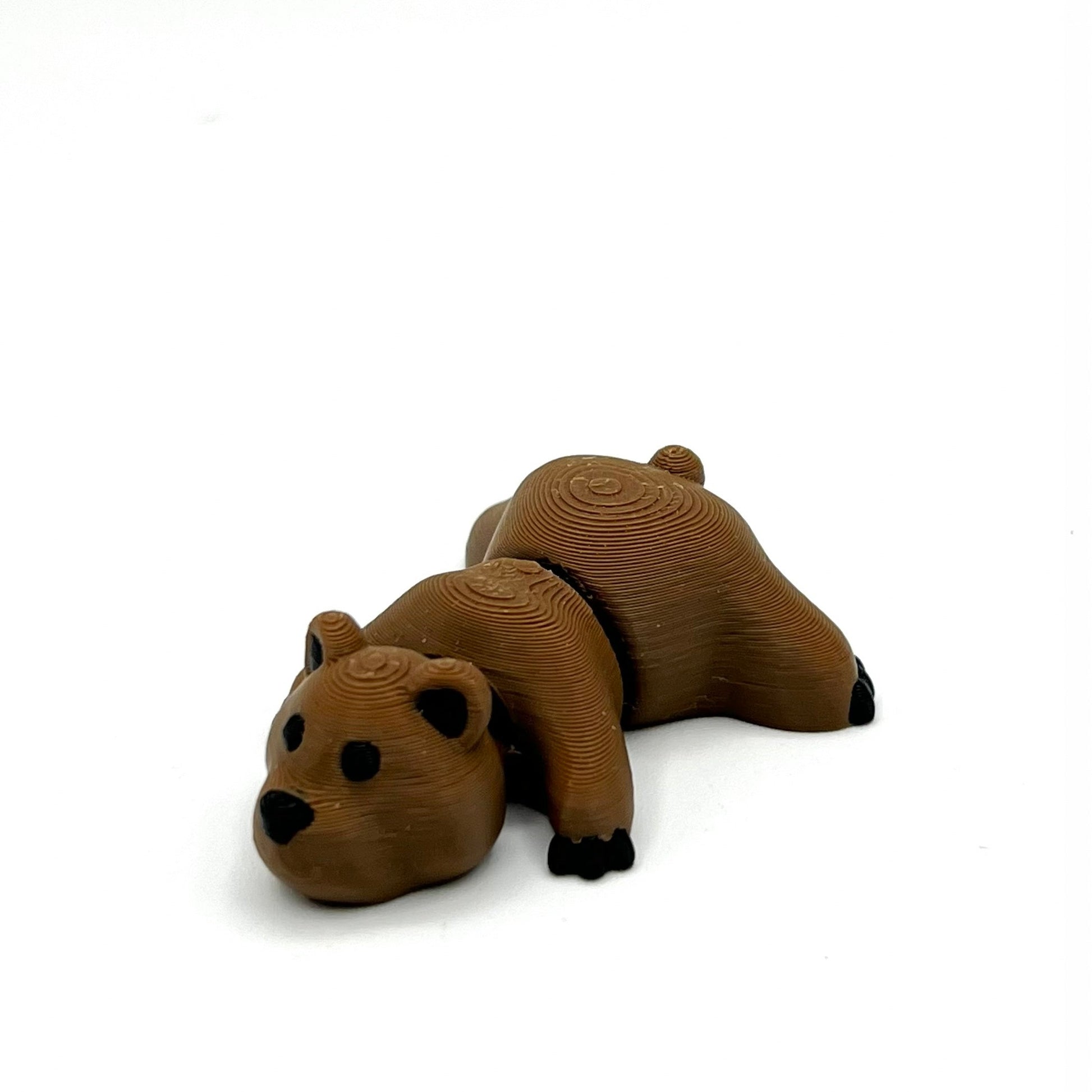 A small brown bear figurine posed on its stomach, photographed on a plain white background.
