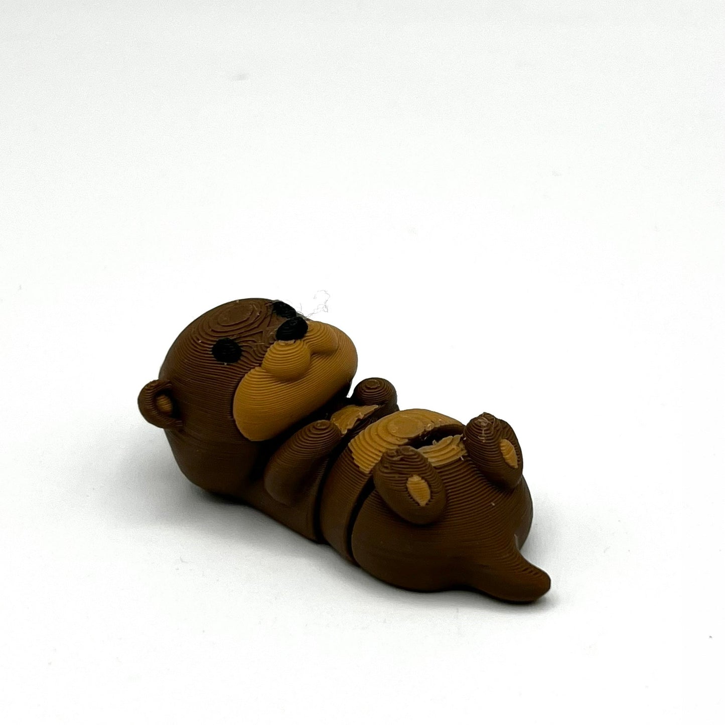A small brown otter figurine lying on its back, photographed on a plain white background.