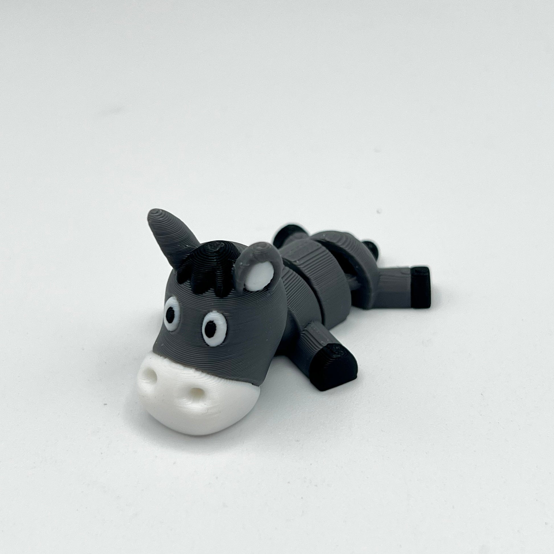 A small gray donkey figurine with a white muzzle and black ears, lying down on a plain white background.