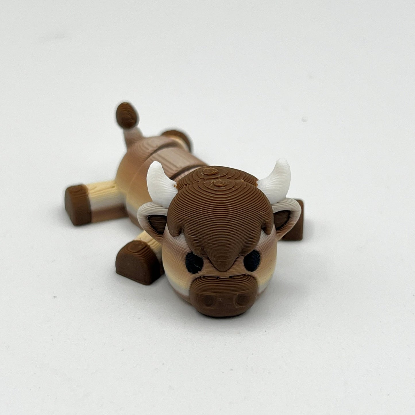 A small brown and beige bull figurine with white horns, photographed on a plain light background.