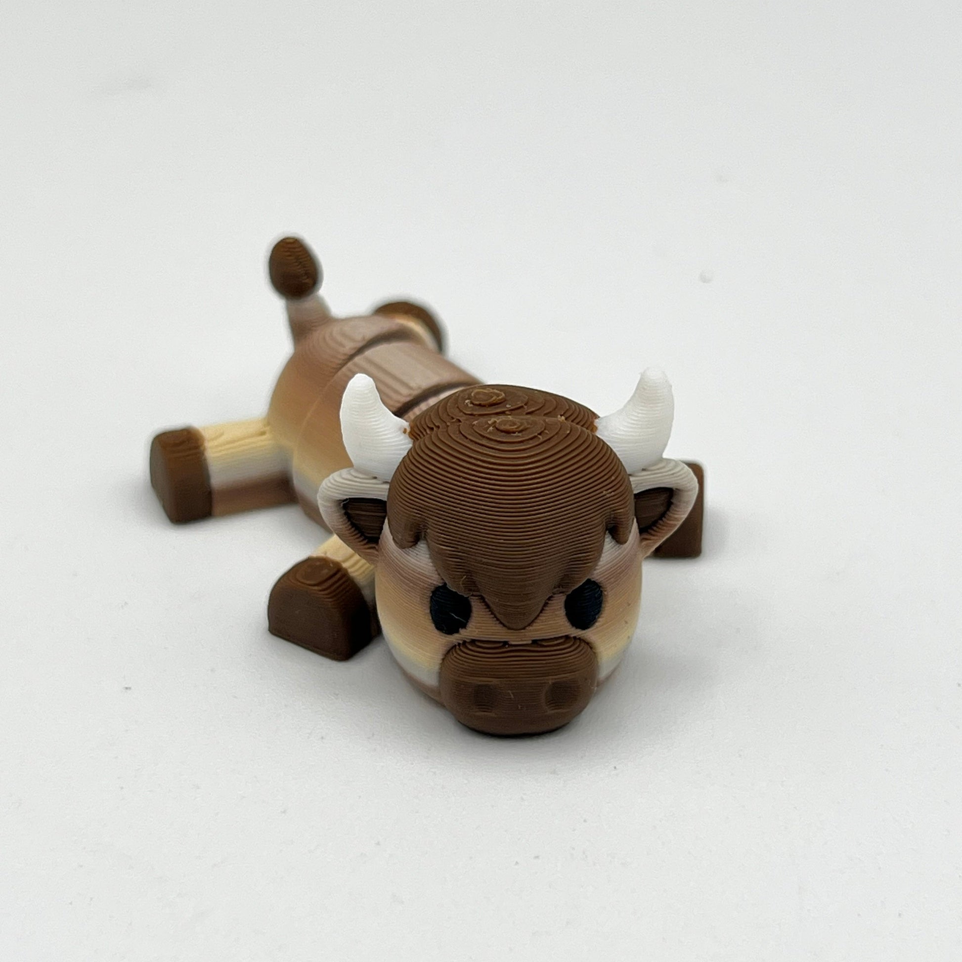 A small brown and beige bull figurine with white horns, photographed on a plain light background.