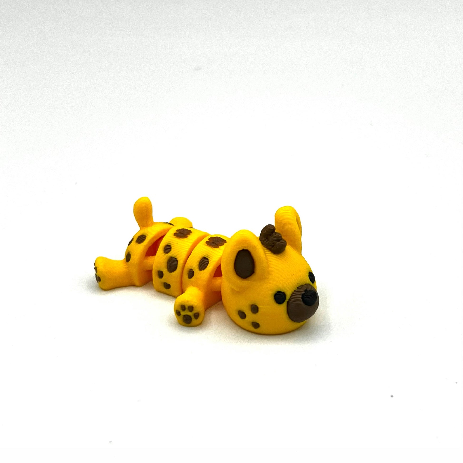 A small yellow toy dog figurine with black spots, lying on its side against a plain white background.