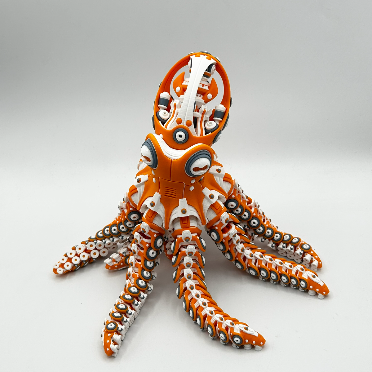 An orange and white 3D-printed octopus toy with detailed black and silver suction cups on its tentacles, photographed on a seamless light gray background.