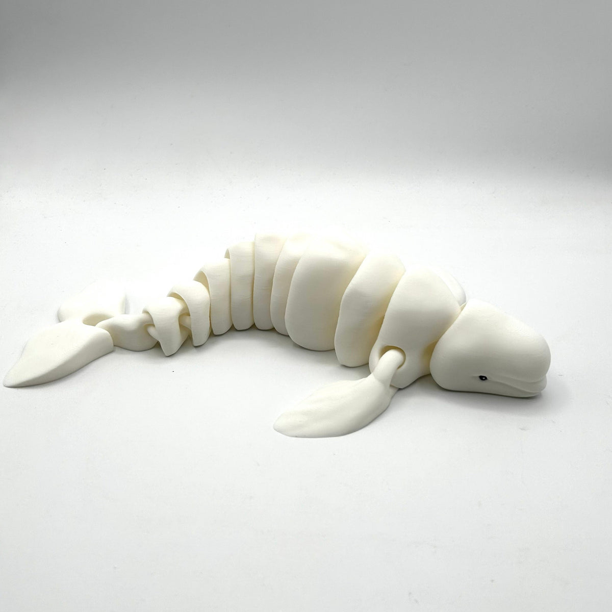 A white articulated beluga whale figurine made of a smooth, matte material, posed on a seamless light gray studio background.