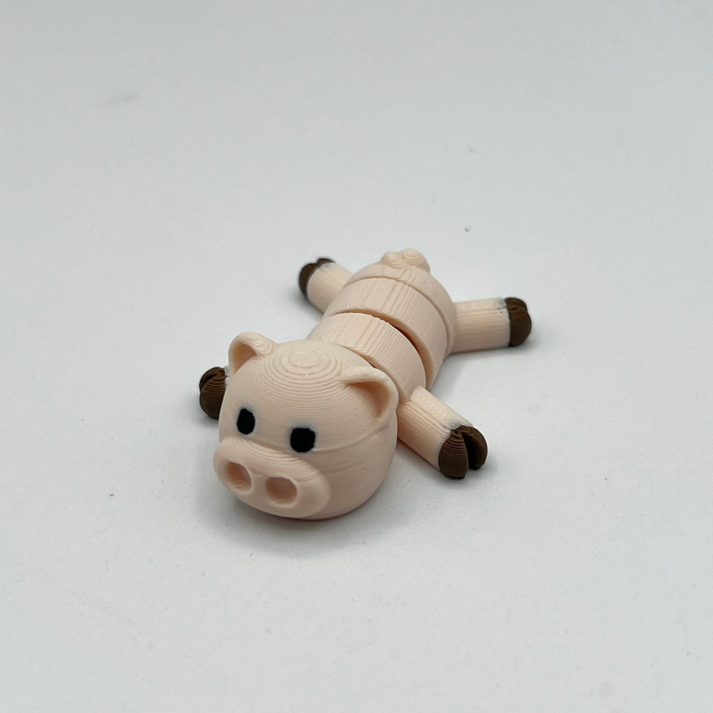 A small pig-shaped novelty item, possibly a USB flash drive or compact disc, lying on its side. The body is a light beige/cream color with dark brown hooves and snout, and small black eyes, set against a plain light gray background.
