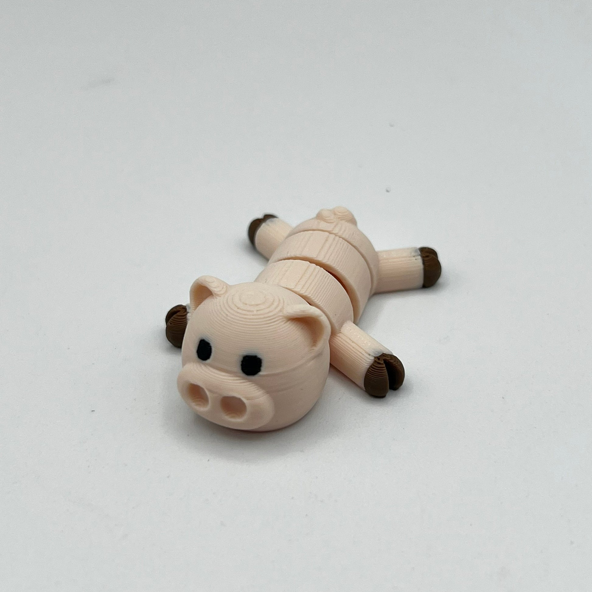 A small pig-shaped novelty item, possibly a USB flash drive or compact disc, lying on its side. The body is a light beige/cream color with dark brown hooves and snout, and small black eyes, set against a plain light gray background.