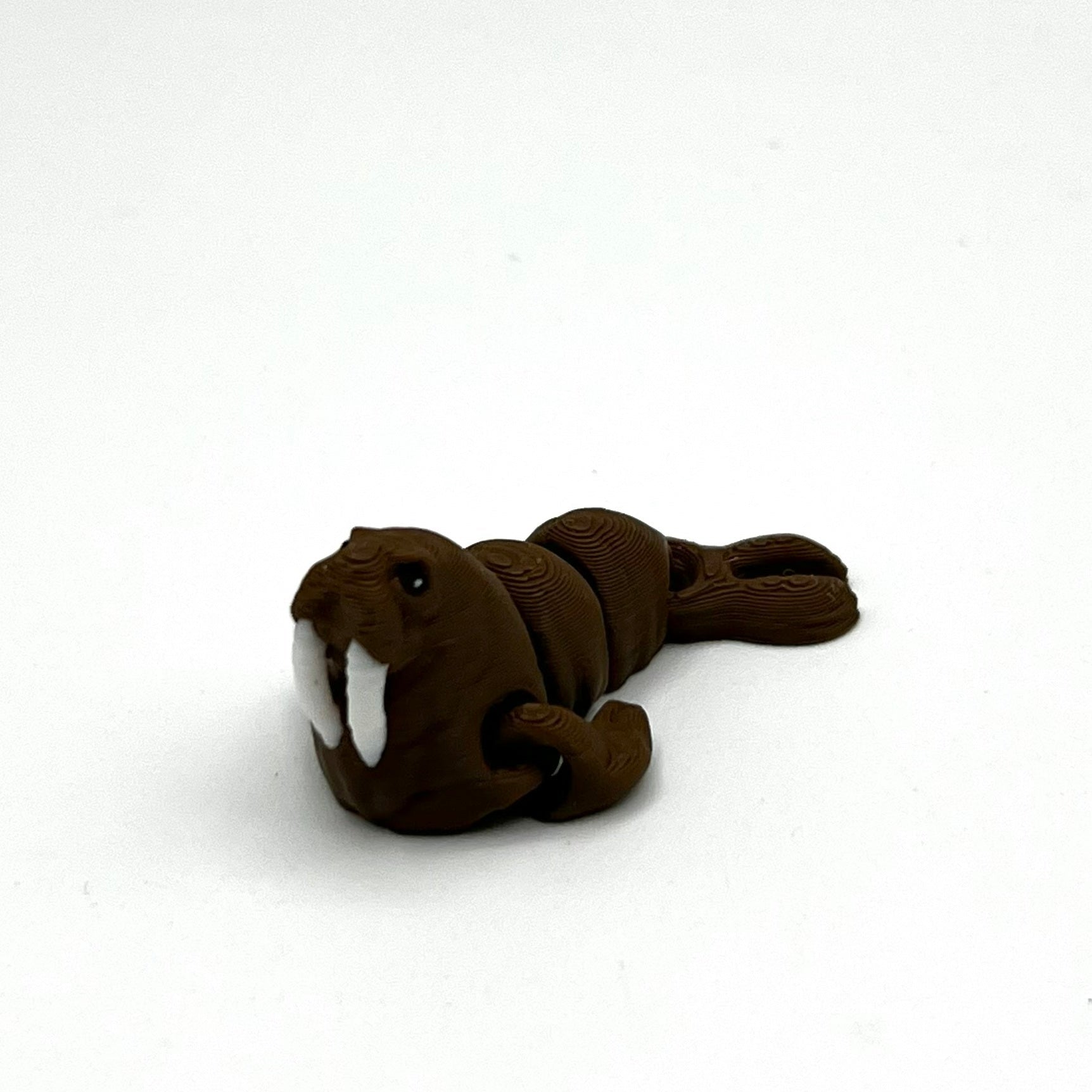 A small brown walrus figurine with white tusks, photographed on a plain white background.